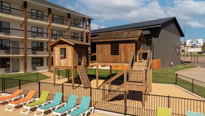 Un parque infantil con estructuras de juego de madera y un edificio con un cartel de un complejo turístico.
