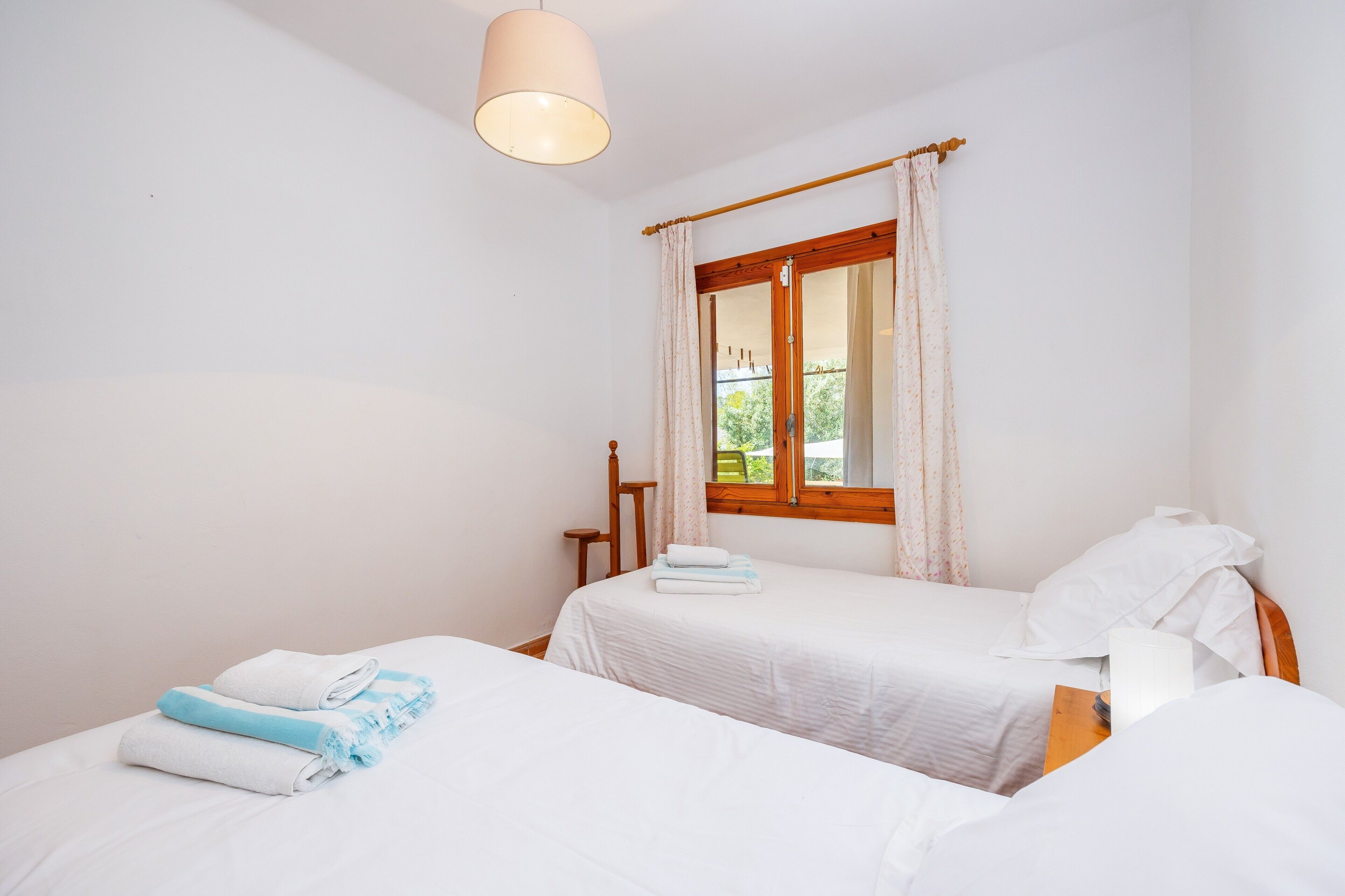 Une chambre avec deux lits, une fenêtre avec des rideaux, une chaise en bois et une table de chevet.