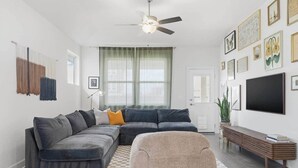Ein modernes Wohnzimmer mit einem Ecksofa, einem kleinen Sessel, einer Holzbank und einem großen Fernseher.