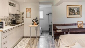 Una cucina compatta con elettrodomestici moderni, un'area pranzo con tavolo e panchetta in legno, e un letto con copriletto beige.