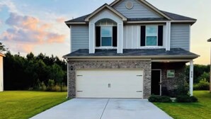A two-story house with a garage, a driveway, and a well-maintained lawn. - Cozy 4BR + Fast WiFi + Self Check-In + Near I-75 (McDonough)