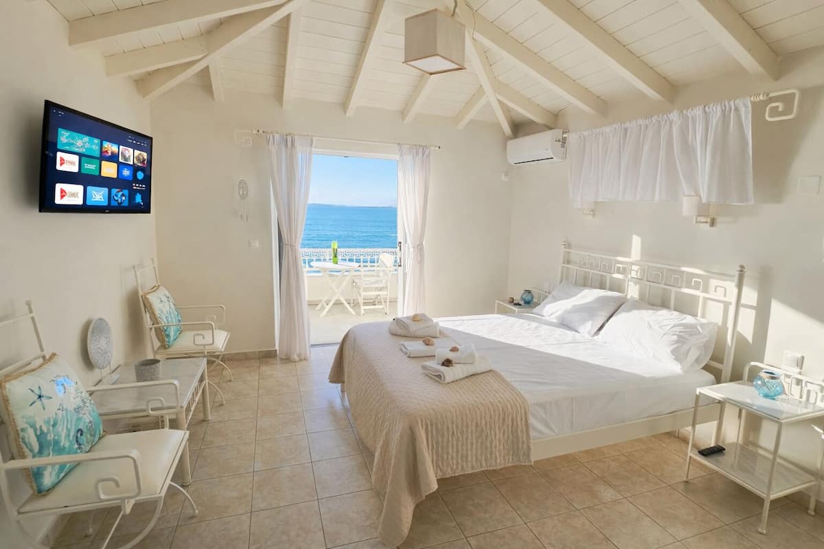 A hotel room with a bed, a TV, a balcony with a view of the sea, and a white color scheme.