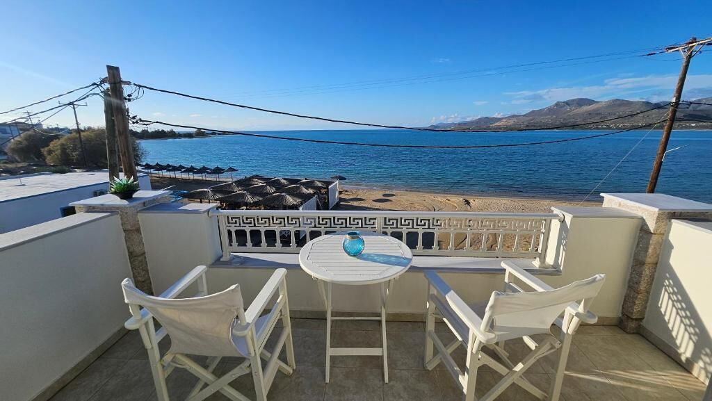 A balcony with a table and chairs overlooking a beach and sea.