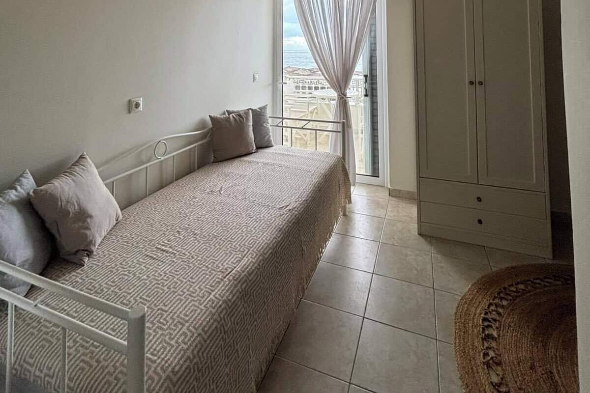 A bedroom with a bed, a wardrobe, a window with curtains, and a view of the sea.