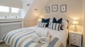 A bedroom with a bed, pillows, a bedside table, a lamp, and a window with a view. - Paddock View (Cheltenham)