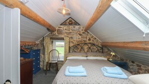Un dormitorio acogedor en el ático, con pared de piedra, techo de madera, una cama con toallas dobladas, una silla y una mesita con lámpara.