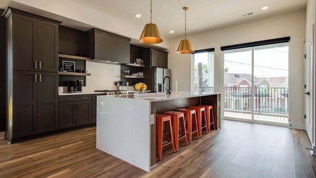 A modern kitchen with dark cabinets, a central island with stools, pendant lighting, and a large sliding glass door to the outdoors. - House of Rock! Ping Pong - 6 beds. Lux home! (Nashville)