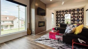 A modern living room with a large window, a black sofa, a red coffee table, and a wall decorated with vinyl records. - House of Rock! Ping Pong - 6 beds. Lux home! (Nashville)