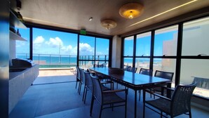 Ein moderner Essbereich mit großem Tisch und Stühlen, großen Fenstern mit Meerblick und einer Decke mit Einbautenleuchten.