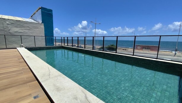 Ein rechteckiger Swimmingpool mit klarem, blauem Wasser, umgeben von einer Holzterrasse und einem Metallgeländer.