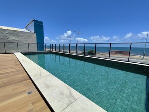 Ein rechteckiger Swimmingpool mit klarem, blauem Wasser, umgeben von einer Holzterrasse und einem Metallgeländer.