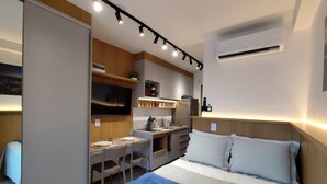 Ein modernes Hotelzimmer mit Bett, Schreibtisch, Stuhl, Fernseher und einer Küchenzeile.