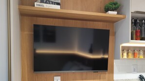 Eine moderne Küche mit Flachbildfernseher an der Wand, einem Holzregal darüber und einem kleinen Topfpflanzen.