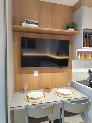 Eine moderne Küche mit Flachbildfernseher an der Wand, einem Holzregal darüber und einem kleinen Topfpflanzen.