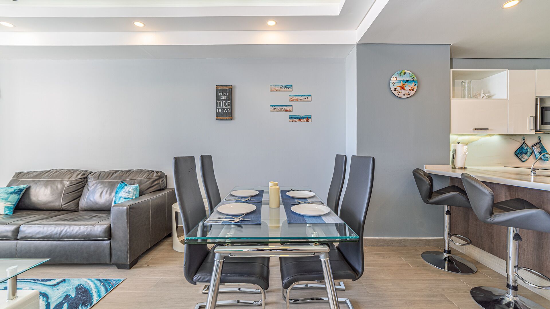Un comedor moderno con una mesa de vidrio, sillas negras y un sofá gris con cojines azules.