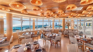 Un restaurante con mobiliario de mimbre, amplias ventanas y vista al océano.