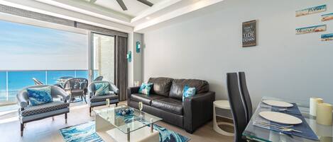 A modern living room with a leather sofa, glass coffee table, and a dining area with a glass table and chairs.