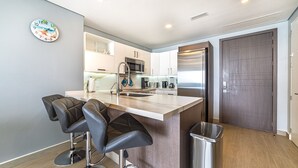 Una cocina moderna con una isla central, taburetes de bar, electrodomésticos de acero inoxidable y un cubo de basura.