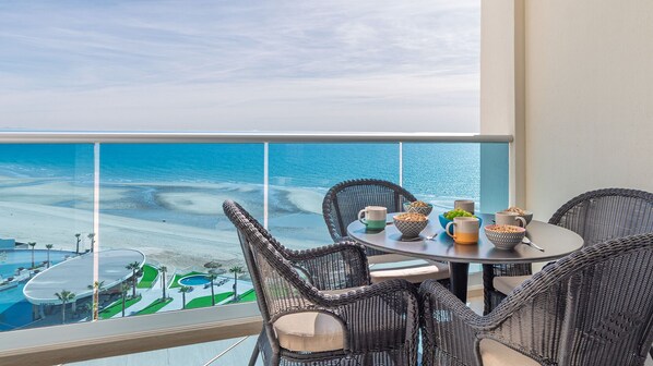 A balcony with wicker furniture, a round table, and bowls of food. - Sublime 1 Bedroom Condo Encantame Towers Verano 903 (Puerto Peñasco)
