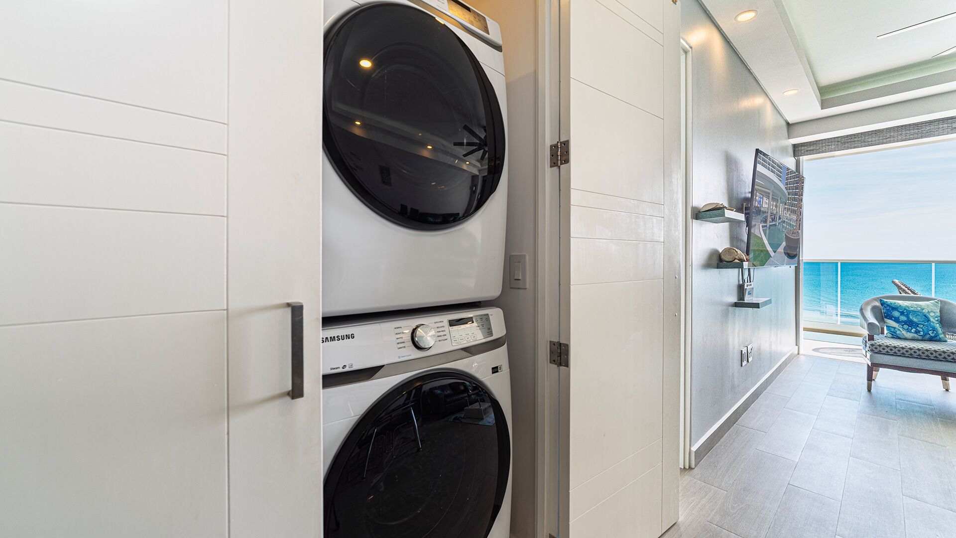 A laundry room with two stacked washing machines, a view of the ocean, and a balcony with a sofa.