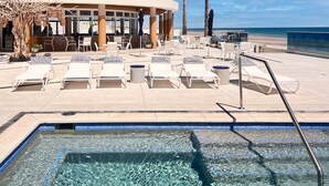 Ett område vid poolen med solstolar, en pool och en byggnad med stora fönster.