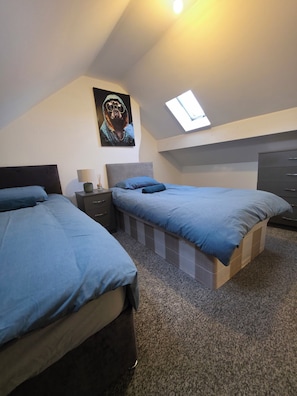 A bedroom with two beds, a nightstand, a dresser, and a skylight. - Alphonsus Home in Middlesbrough Town (Middlesbrough)