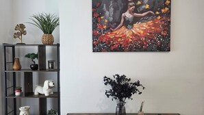 Un salon avec un meuble en bois foncé, un vase blanc contenant des fleurs noires et un tableau représentant une femme portant une robe colorée.