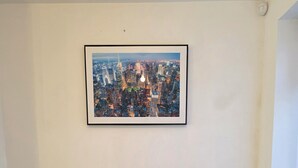 Un coin repas comprenant une table, quatre chaises, un radiateur et un tableau encadré représentant un paysage urbain accroché au mur.
