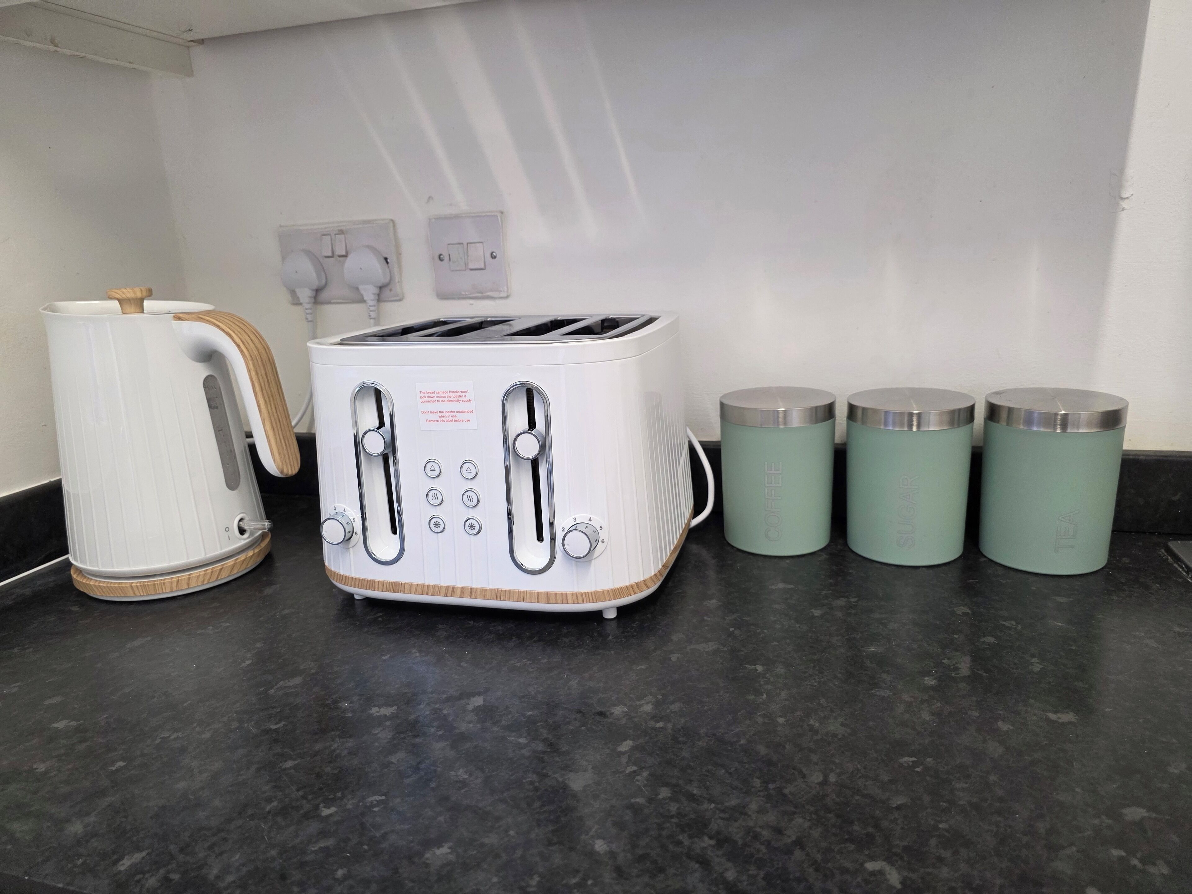 A kitchen with a white toaster, a white kettle, and three teal containers labeled coffee, sugar, and tea.
