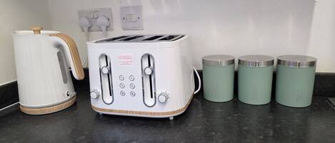 A kitchen with a white toaster, a white kettle, and three teal containers labeled coffee, sugar, and tea.