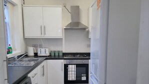 Une cuisine compacte avec des meubles blancs, un four encastré, un lave-linge et un réfrigérateur.