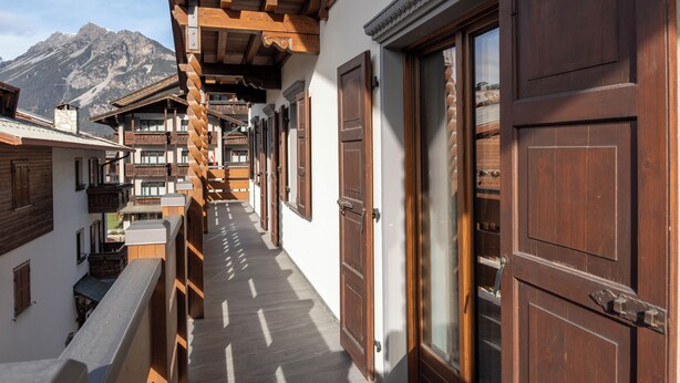 Un corridoio stretto con balconi in legno e ampie porte di legno, con montagne sullo sfondo.