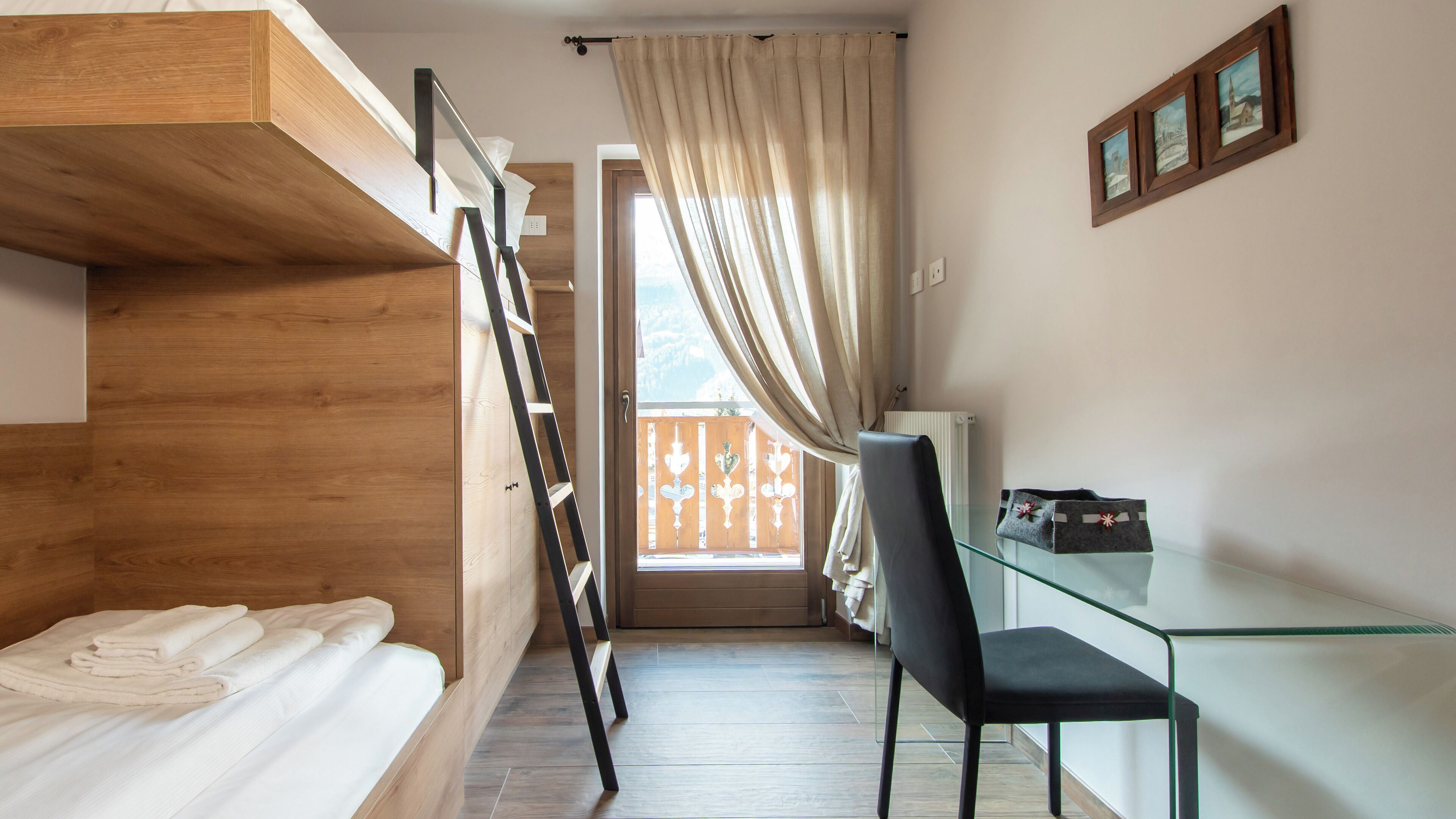 A compact room with a bunk bed, a desk with a chair, and a window with curtains.