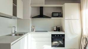 Una cucina moderna con mobili bianchi, un lavello in acciaio inossidabile, una cappa aspirante nera, un forno a microonde, un bollitore ed un forno integrato.