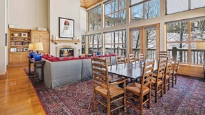 A spacious living area with a fireplace, large windows, and a dining table with chairs. - Greystone 60 Five Bedroom (Beaver Creek)