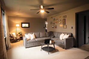 A modern living room with a grey sectional sofa, a round coffee table, and a ceiling fan.