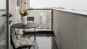 A balcony with a small table and chair, a vase with flowers, and a view of buildings in the distance. - Modern Flat with Balcony & Garage by HostWise (Porto)