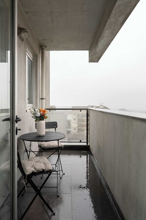 A balcony with a small table and chair, a vase with flowers, and a view of buildings in the distance. - Modern Flat with Balcony & Garage by HostWise (Porto)