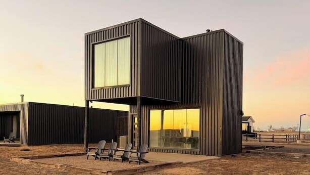 Un bâtiment moderne à deux étages, doté de grandes fenêtres et d’un toit plat, situé dans un champ ouvert et aride.
