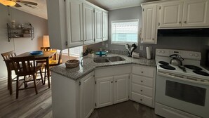 A kitchen with white cabinets, a granite countertop, a stove, and a dining area with a table and chairs. - Serenity House for Two! (Kissimmee)