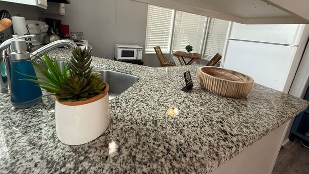 A kitchen with granite countertops, a sink, a microwave, and a dining area with a table and chairs. - Serenity House for Two! (Kissimmee)