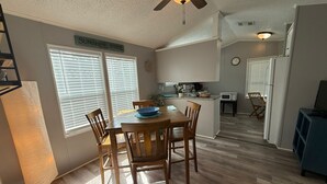 A dining area with a wooden table and chairs, a kitchen in the background, and a ceiling fan. - Serenity House for Two! (Kissimmee)