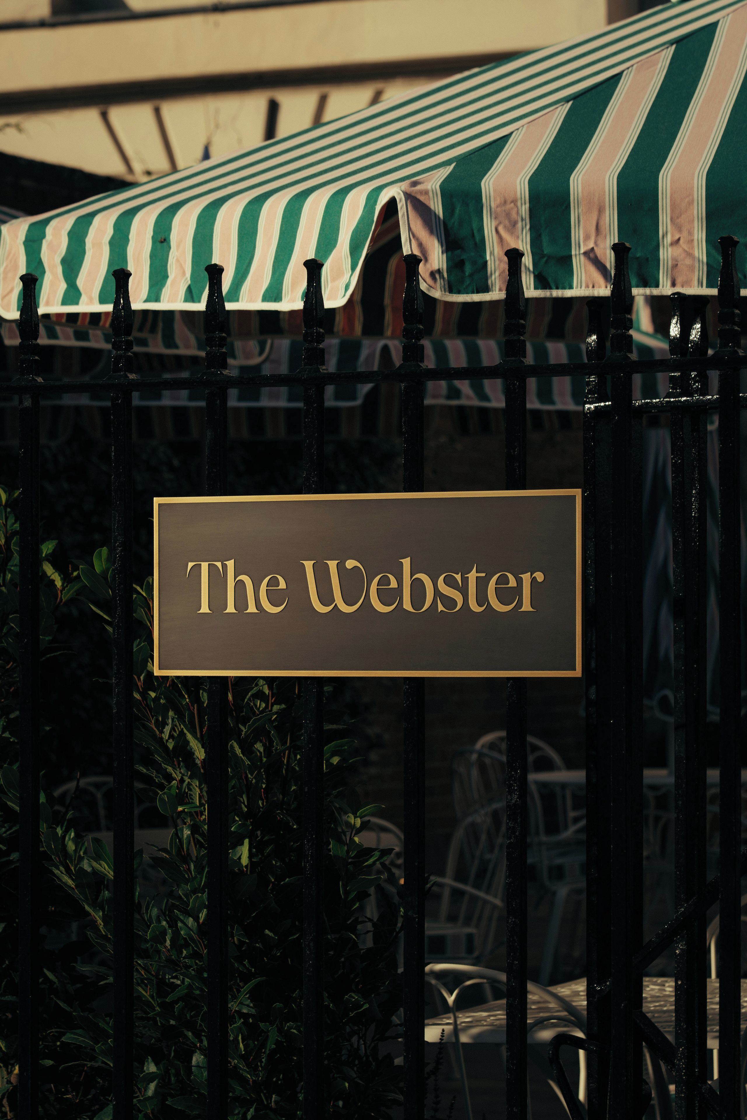 A sign with the text 'The Webster' on a metal fence.