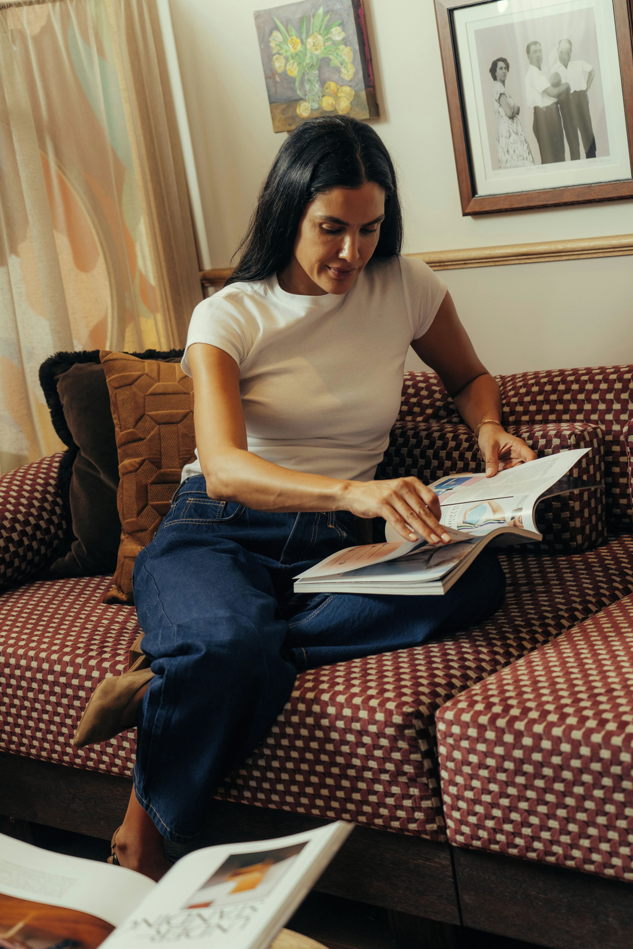 A person sitting on a patterned sofa with a book, in a room with a framed picture on the wall.