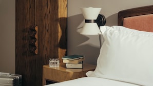 A neatly made bed with a pillow, a bedside table with a lamp, a book, and a glass of water.