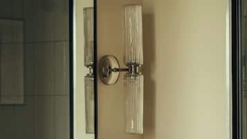 A bathroom with a mirror, two wall-mounted light fixtures, a sink with a white countertop, and a glass soap dish.