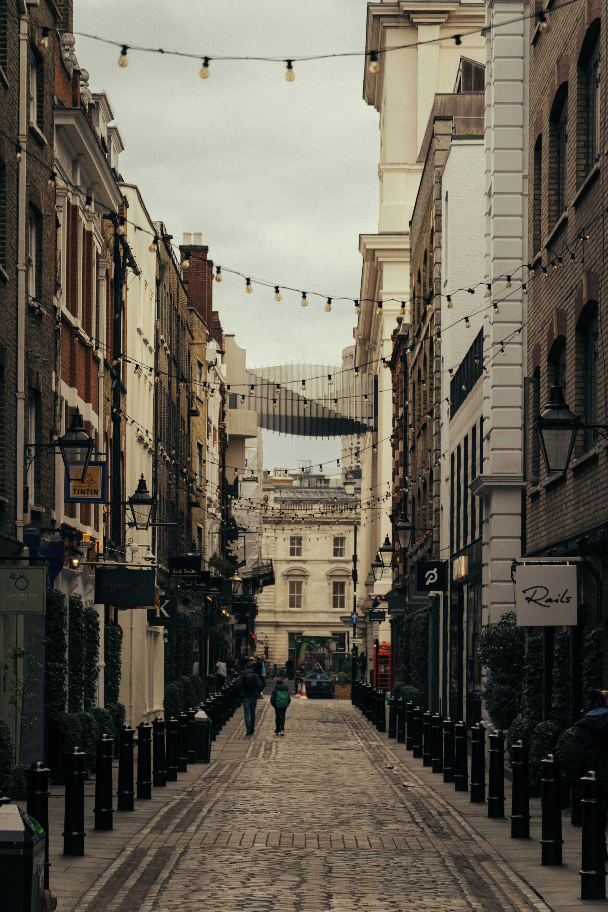 A cobblestone street lined with historic buildings, some with visible signage, and a string of lights above.