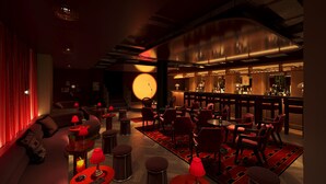 A dimly lit bar area with red seating, a bar counter, and a large circular light fixture.