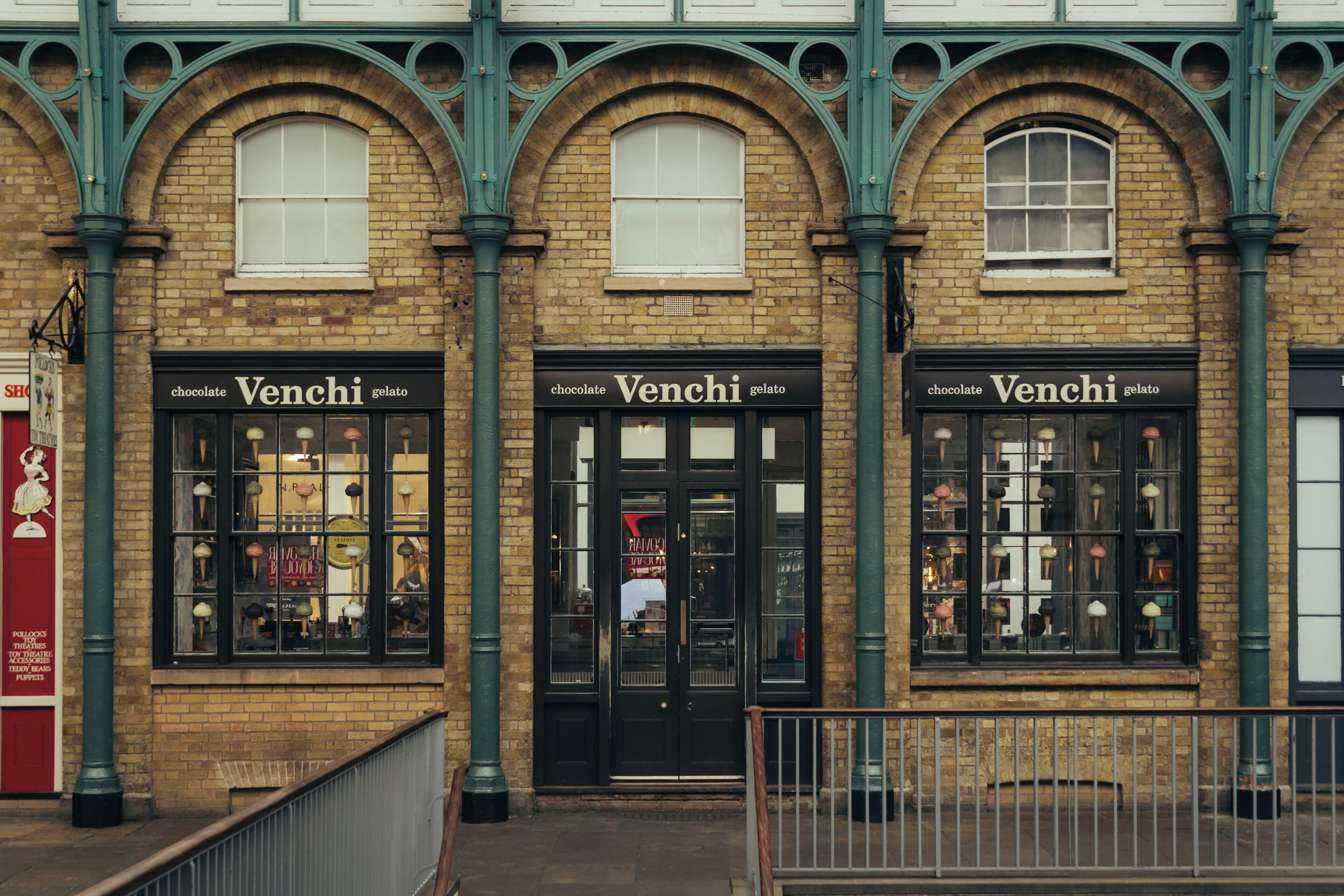 A brick building with three storefronts labeled 'Venchi' and a sign for 'Polly's Puppets.'