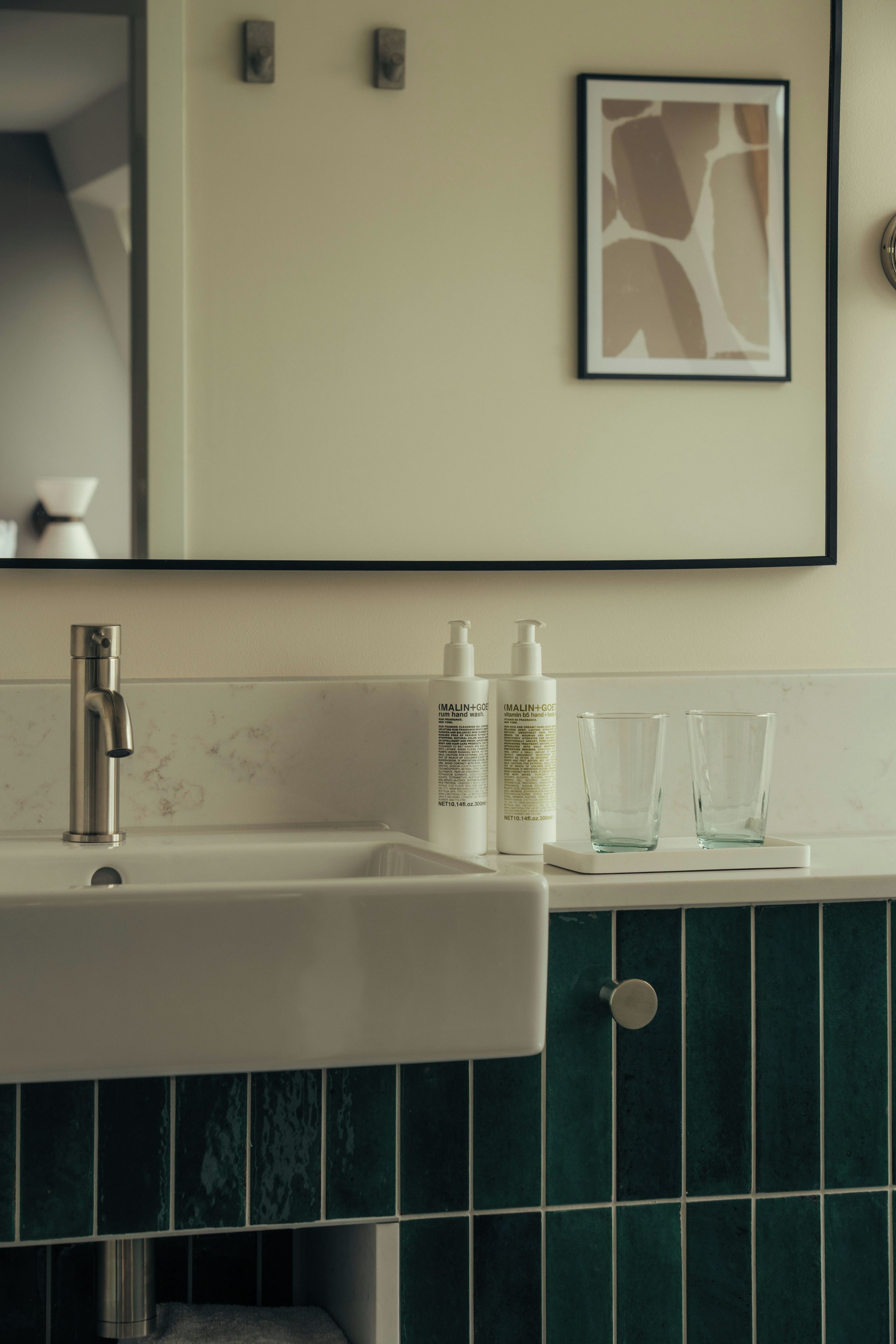 Une salle de bain avec un lavabo blanc, deux flacons de savon liquide et deux verres posés sur une étagère blanche.